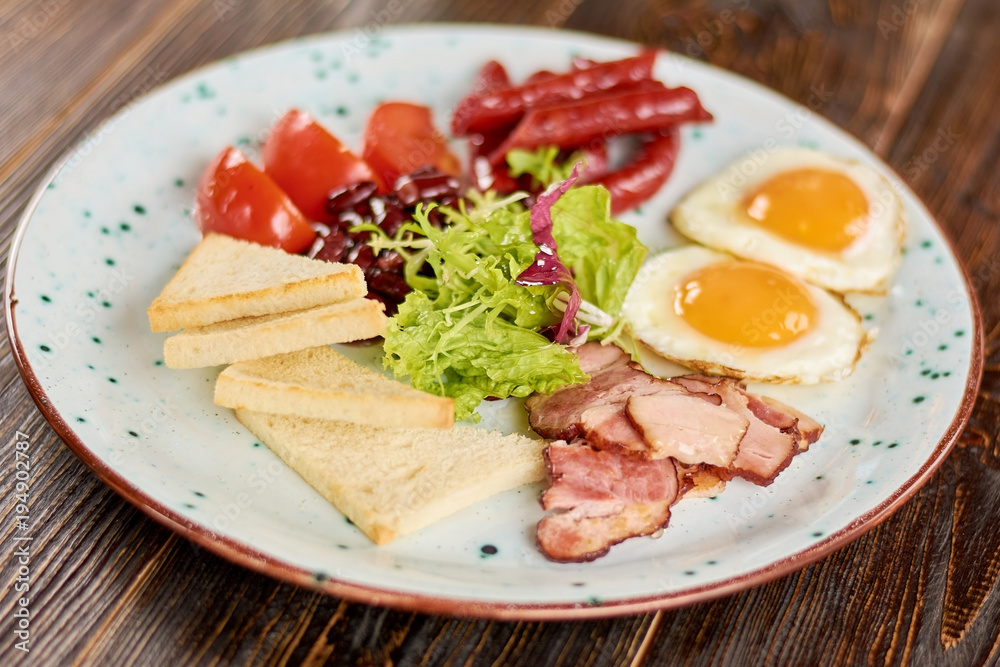 English breakfast served with green salad. English breakfast with fried eggs, baked sausages and bacon, tomatoes, beans and toasts. Traditional british breakfast. English breakfast served with green salad. English breakfast with fried eggs, baked sausages and bacon, tomatoes, beans and toasts. Traditional british breakfast.