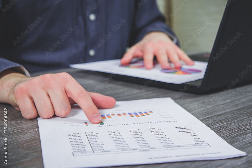 Work in the office, at the desk, data analysis. The man checks the data on the charts, the analysis of costs, profits. Annual balance. The businessman controls expenses and disposes of money. Work in the office, at the desk, data analysis. The man checks the data on the charts, the analysis of costs, profits. Annual balance. The businessman controls expenses and disposes of money.