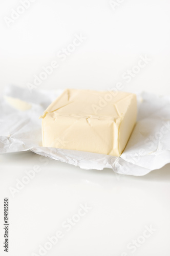Typical German block of unsalted butter weighing 250 grams unwrapped on grease-proof wrapping paper on white background