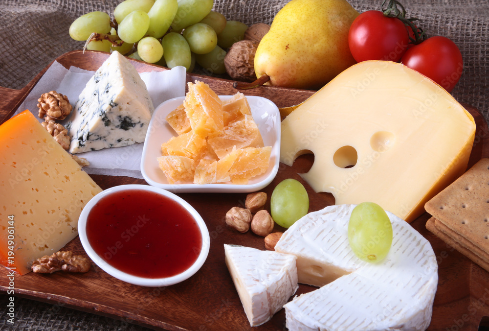 Assortment of cheese with fruits, grapes and nuts on a wooden serving tray.
