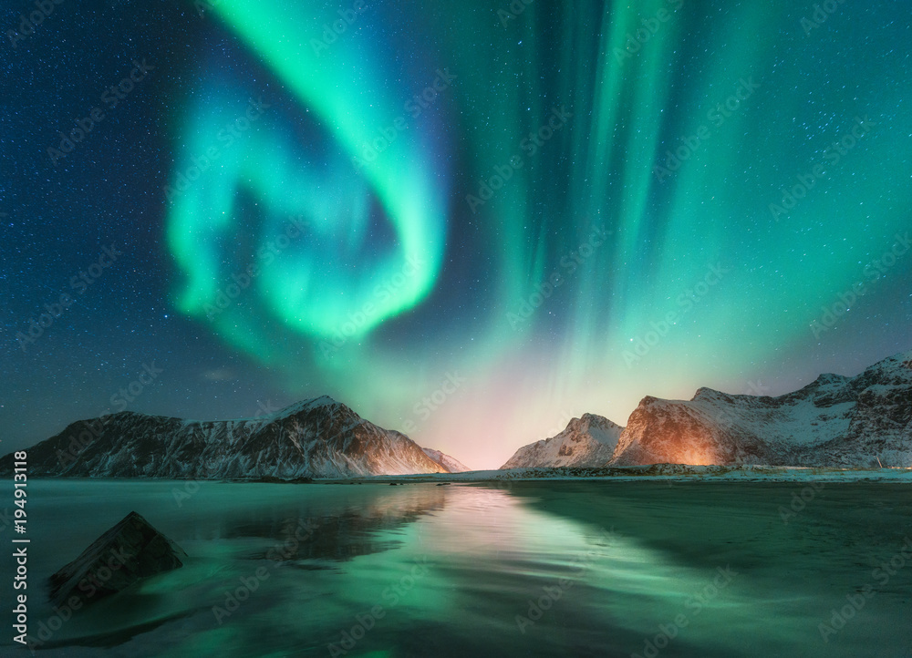 Fototapeta Zorzy borealis w Lofoten wyspach, Norwegia. Zorza polarna. Zielone zorza polarna. Gwiaździste niebo z polarnymi światłami. Noc zimowy krajobraz zorza polarna, morze odbicie nieba, kamienie, plaża i ośnieżone góry