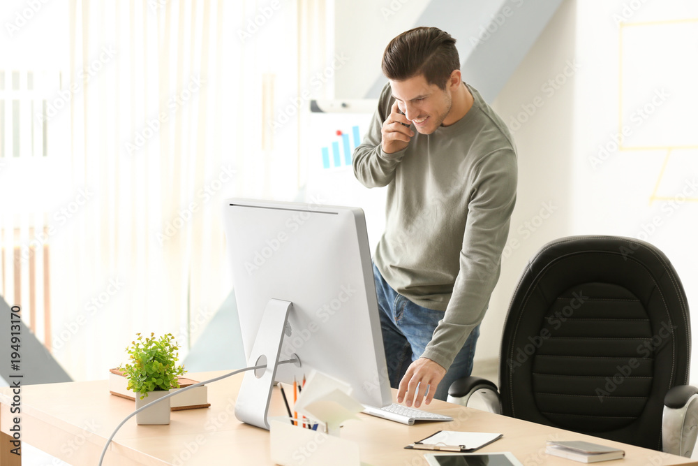 Young man talking on mobile phone while working in office Young man talking on mobile phone while working in office