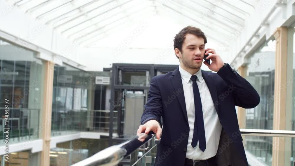 Happy attractive young businessman walking and using mobile phone indoors. Happy attractive young businessman walking and using mobile phone indoors.