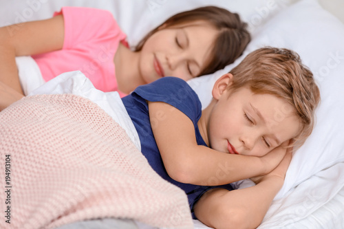 Cute little brother and sister sleeping in bed at home