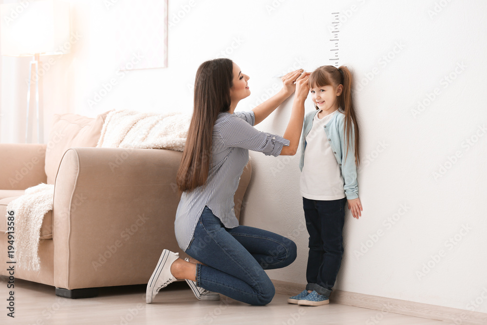 Young woman measuring her daughter's height indoors - obrazy, fototapety, plakaty 