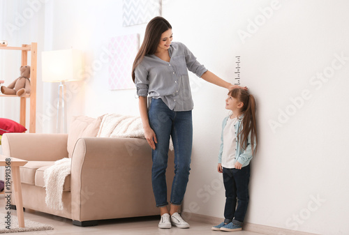 Young woman measuring her daughter's height indoors photo