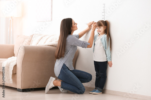 Quadro su tela Young woman measuring her daughter's height indoors