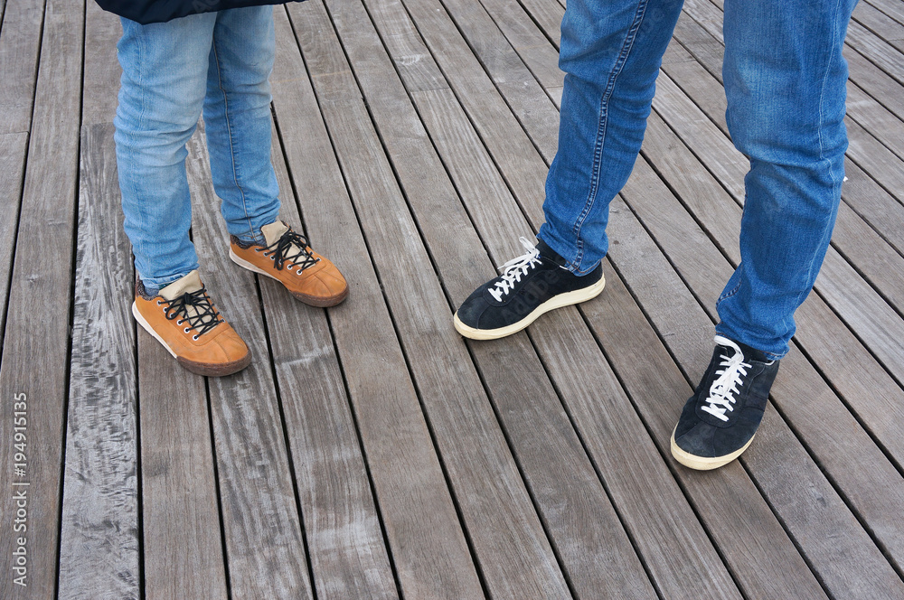 Child's and man's feet. Jeans and shoes on wooden floor