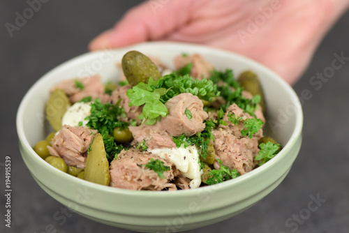 A hand holding a bowl of healthy tuna salad on dark background- closeup