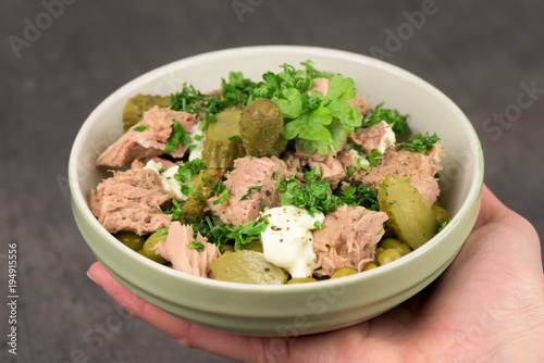 A hand holding a bowl of healthy tuna salad on dark background- closeup