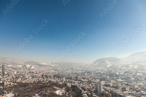 Aerial view of Sarajevo during a sunny winter afternoon  covered in snow. The historical center with its mosques and minarets can be seen in background