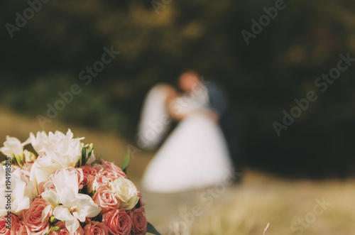 wedding bouquet laying on the grass with blurred wedding couple