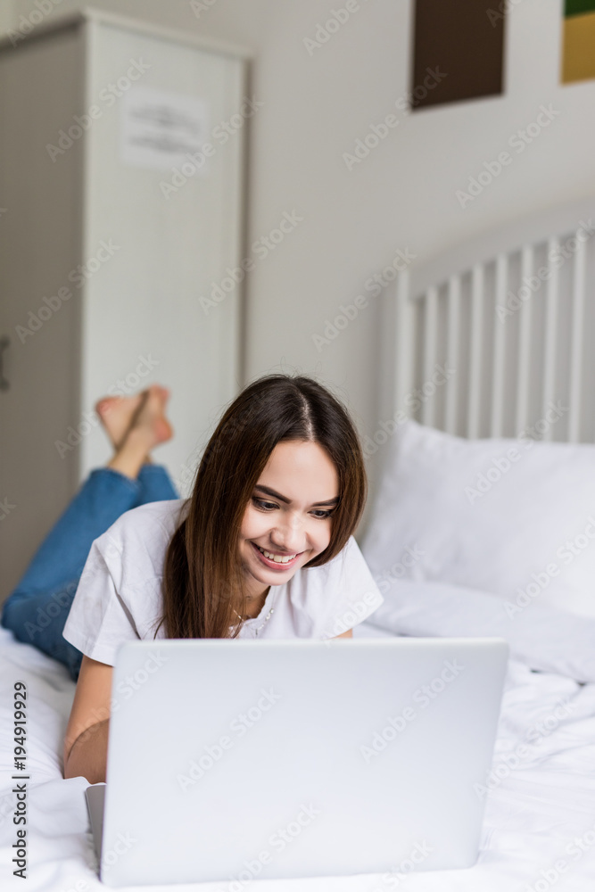 Smiling woman with her legs raised slightly in front of her laptop lying on the bed. Smiling woman with her legs raised slightly in front of her laptop lying on the bed.