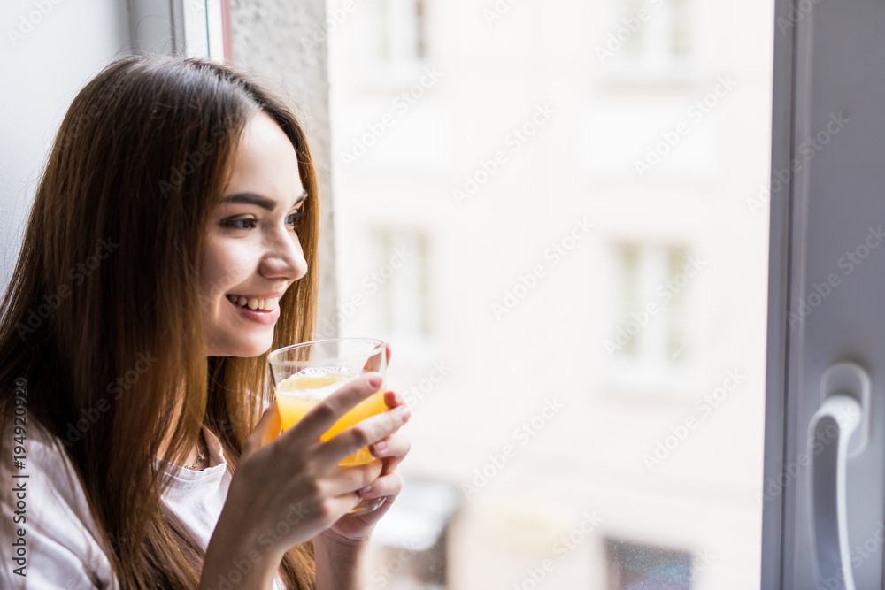 Smiling woman with glass of juice sitting on windowsill Smiling woman with glass of juice sitting on windowsill