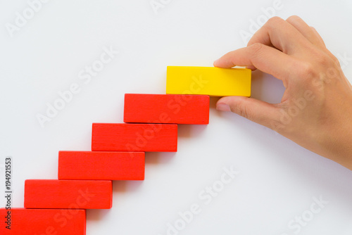 Concept of building success foundation. Women hand put red wooden block on yellow wooden blocks in the shape of a staircase