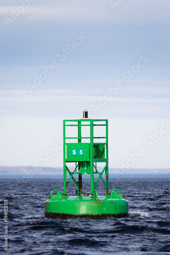 Large green metal marker buoy floating among small waves.