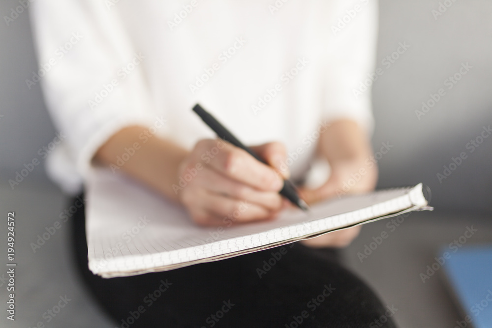 Fototapeta premium blurry closesup of womens hand with a pen writing on a notepad