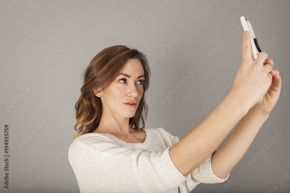 pretty women taking a selfie with a smartphone on gray background pretty women taking a selfie with a smartphone on gray background