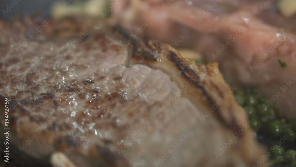 Closeup of delicious beef steaks placed on hot grill with fresh green pepper, fried butter and being heated in a pan - video in slow motion Closeup of delicious beef steaks placed on hot grill with fresh green pepper, fried butter and being heated in a pan - video in slow motion