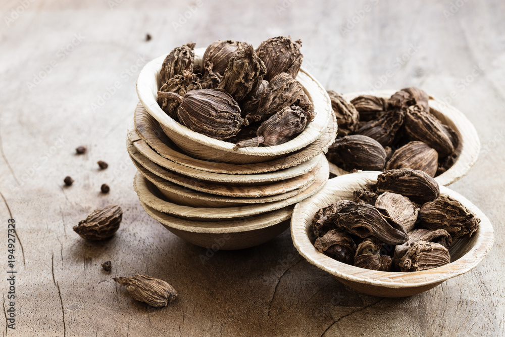 Black cardamom in bowls on wooden background Black cardamom in bowls on wooden background