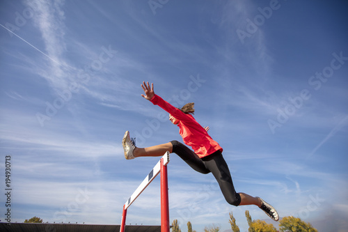 Foto Female athlete jumping above the hurdle during the race