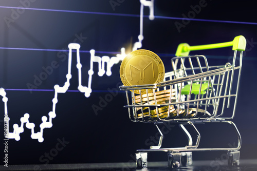 MAKER cryptocurrency; shopping cart (trolley) with gold physical MAKER (MKR) coins on the background of the financial chart