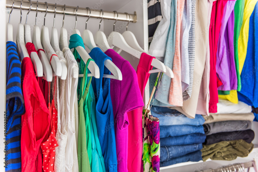 Fashion clothes in walk-in clothing closet or store display for shopping display. Colorful choices of trendy outfits well arranged in clean racks. Spring cleaning concept. Summer home living wardrobe.