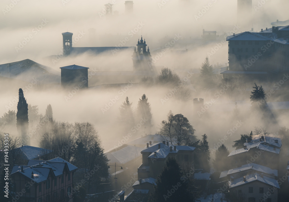 Fototapeta premium Bergamo, Italy. Drone aerial view of an amazing landscape of the fog rises from the plains and covers the old town