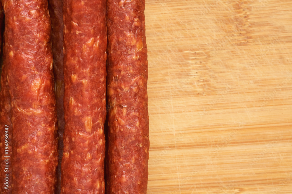 Thin smoked sausage on a wooden background. Close-up. Thin smoked sausage on a wooden background. Close-up.