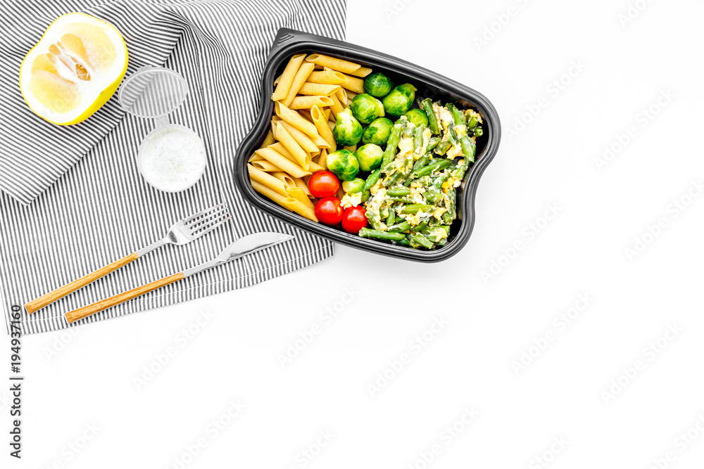 Healthy and hearty lunch for office worker. Vegetables Brussels sprout, cherry tomatoes, knock beans near pasta in plastic container on white background top view copy space