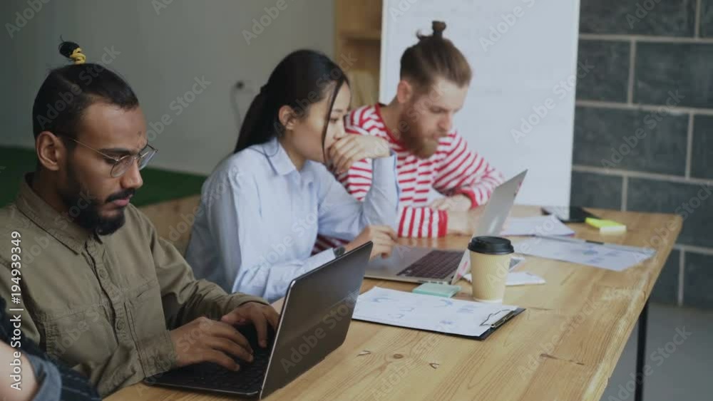 Multi-ethnic team of coworkers working on technology startup project. African american concentrated man typing on laptop computer in loft office Multi-ethnic team of coworkers working on technology startup project. African american concentrated man typing on laptop computer in loft office