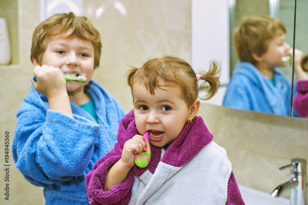 Cute kids in bathrobes in the bathroom brushing their teeth
