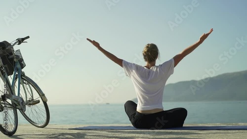 Young girl with bicycle do yoga asana at sea pier at sunrise rapid slow motion
