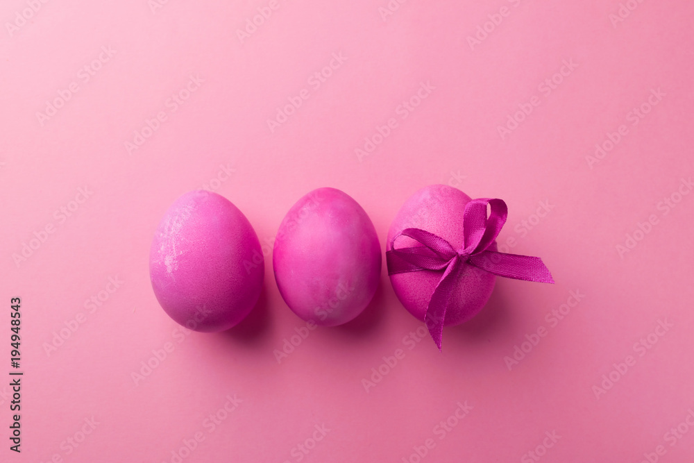 Bright pink eggs with a satin bow on a trendy violet background. Celebratory concept.