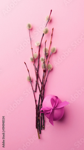  Bright violet egg with a satin bow and pussy-willow branches on a trendy pink background. Celebratory concept.