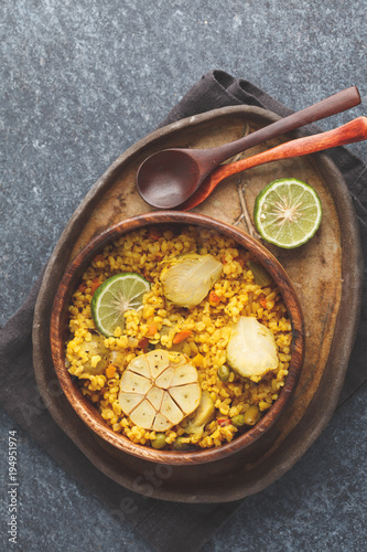 Curry bulgur with vegetables in wooden bowl. Dark background, top view, vegan meal concept.