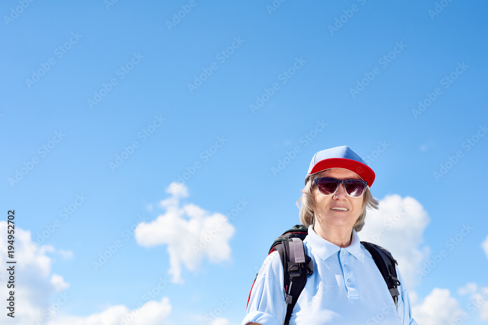 Portrait of active senior woman travelling on hiking trip, posing smiling happily against clear blue sky, copy space Portrait of active senior woman travelling on hiking trip, posing smiling happily against clear blue sky, copy space