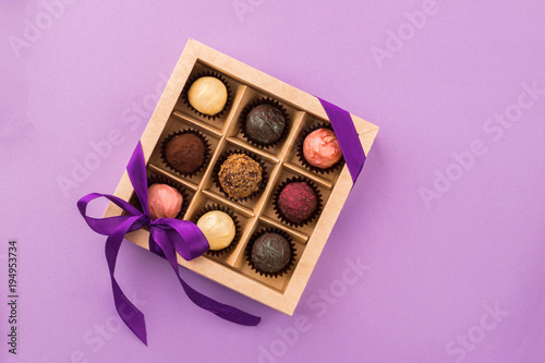 A set of assorted chocolates in a paper box with a satin purple ribbon on a bright background © ximich_natali