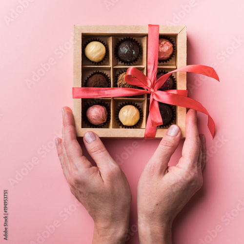  Box with chocolate sweets of different varieties in female hands. The box is decorated with a pink satin ribbon and bow.