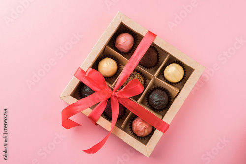 A set of assorted chocolates in a paper box with a satin pink ribbon on a pastel background.Flat layout.