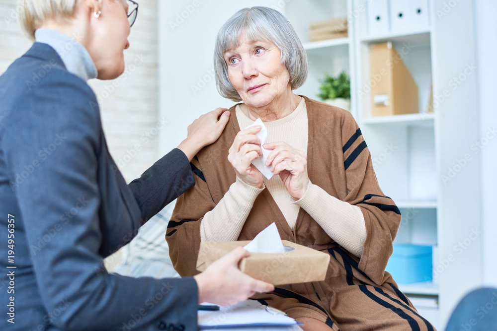 Portrait of depressed elderly woman confining in female psychologist during therapy session, copy space