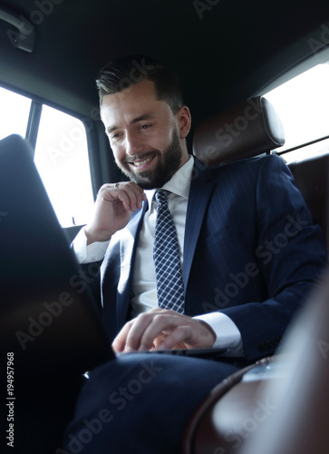 Caucasian male business executive travelling by a car and working on laptop computer. © ASDF