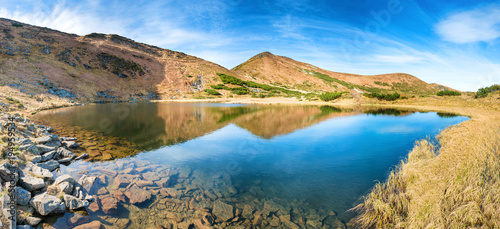 Panorama of mountains lake with reflection in blue water, morning light and shining sun © Pavlo Vakhrushev