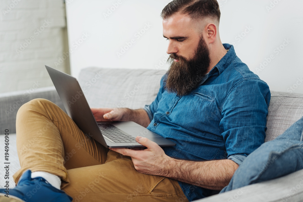 Bearded man sitting on sofa with laptop Bearded man sitting on sofa with laptop