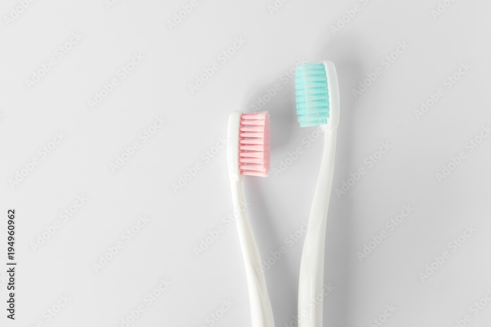 Close up of two plastic white toothbrushes with pink and blue bristle on white background. Free copy space. Close up of two plastic white toothbrushes with pink and blue bristle on white background. Free copy space.