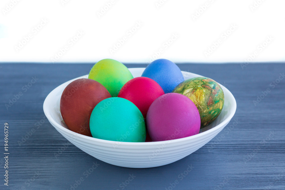 White plate of Easter versicolored eggs on grey wood White plate of Easter versicolored eggs on grey wood