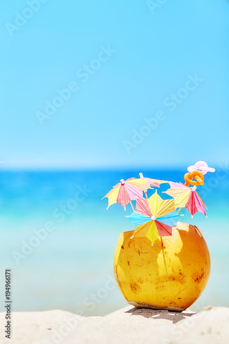 Coconut with colorful umbrellas and straws on a beach, summer fun holiday concept, selective focus, space for text.