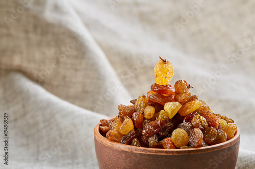 Ceramic bowl with golden raisins on light tablecloth, close-up, selective focus photo