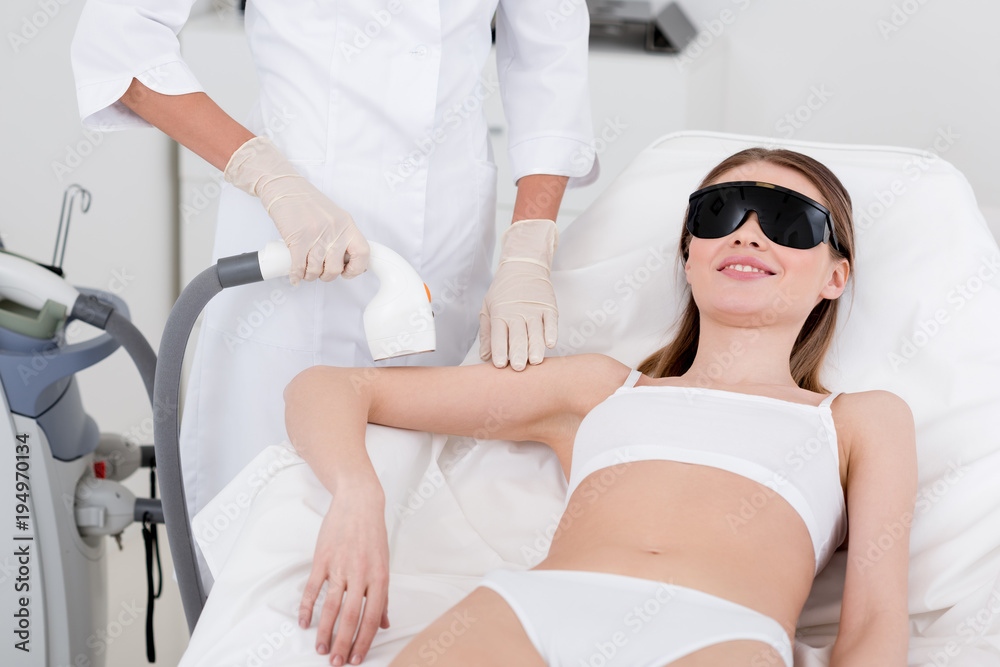 partial view of woman receiving laser hair removal procedure on arm made by cosmetologist in salon partial view of woman receiving laser hair removal procedure on arm made by cosmetologist in salon