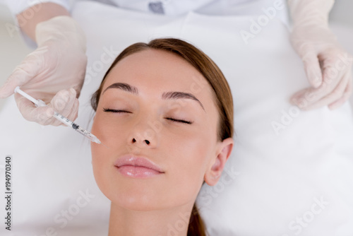 partial view of young woman getting beauty injection made by cosmetologist in salon